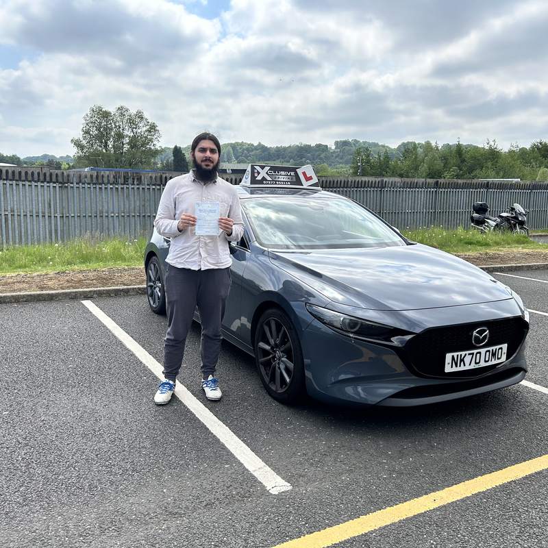 A newly qualified driver with their driving test pass certificate beside the tuition car