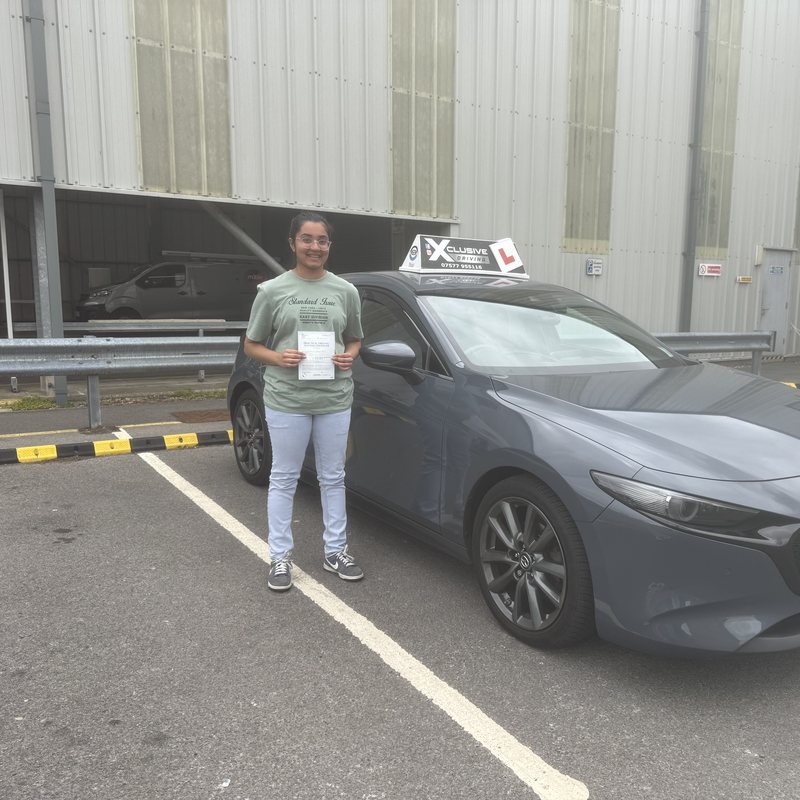 A newly qualified driver holding their pass certificate beside the Xclusive Driving tuition car