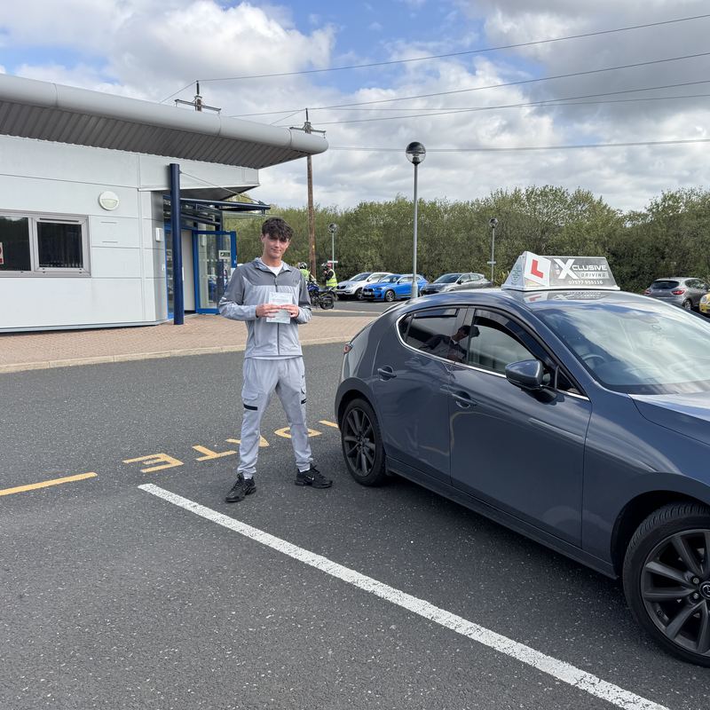 A learner driver with their practical driving test pass certificate beside the Xclusive Driving tuition car